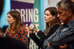 Woman speaking with a Spring Impact banner behind